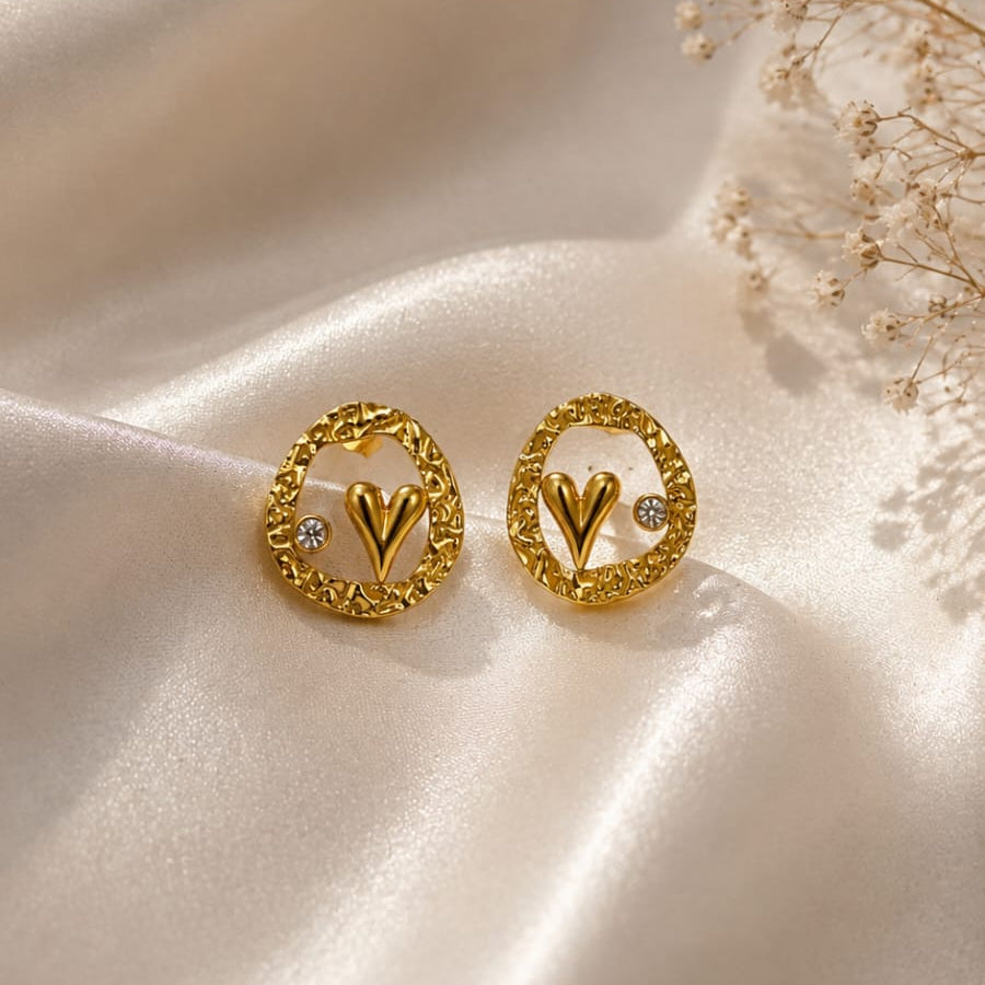 Gold earrings with heart design on a beige fabric background