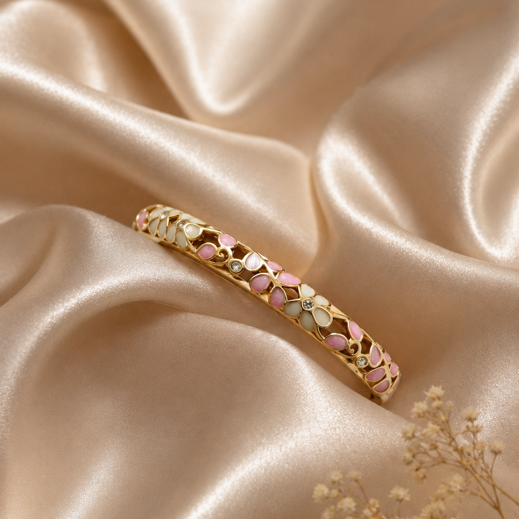 Gold bracelet with pink and green stones on a beige satin background
