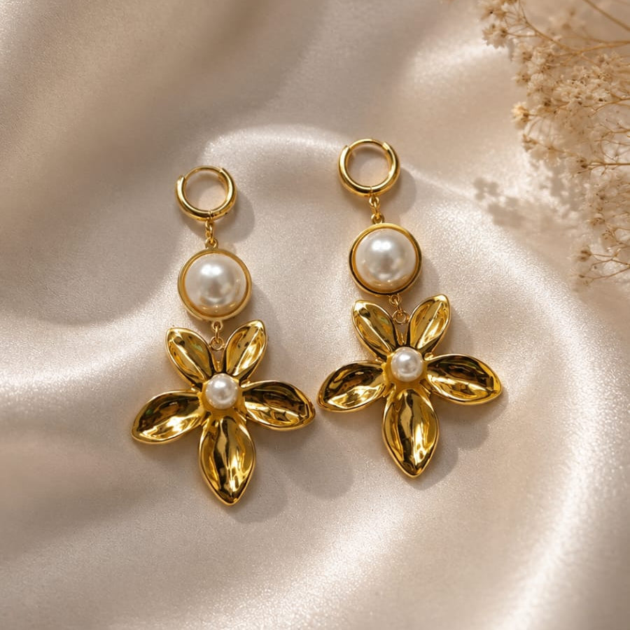 Gold flower-shaped earrings with pearl centers on a beige fabric background
